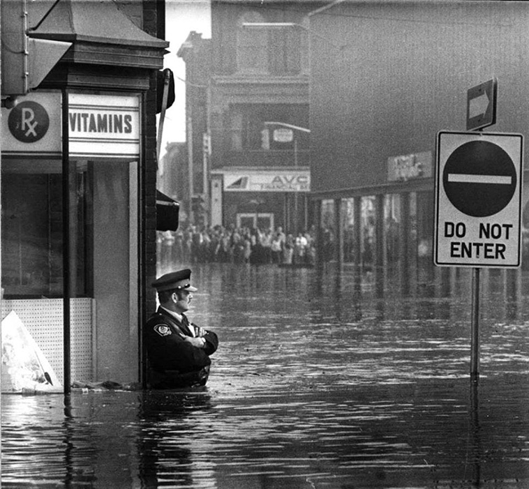 Canadian police officer guarding the pharmacy in waist-high flood waters in Galt, Ontario, 1974