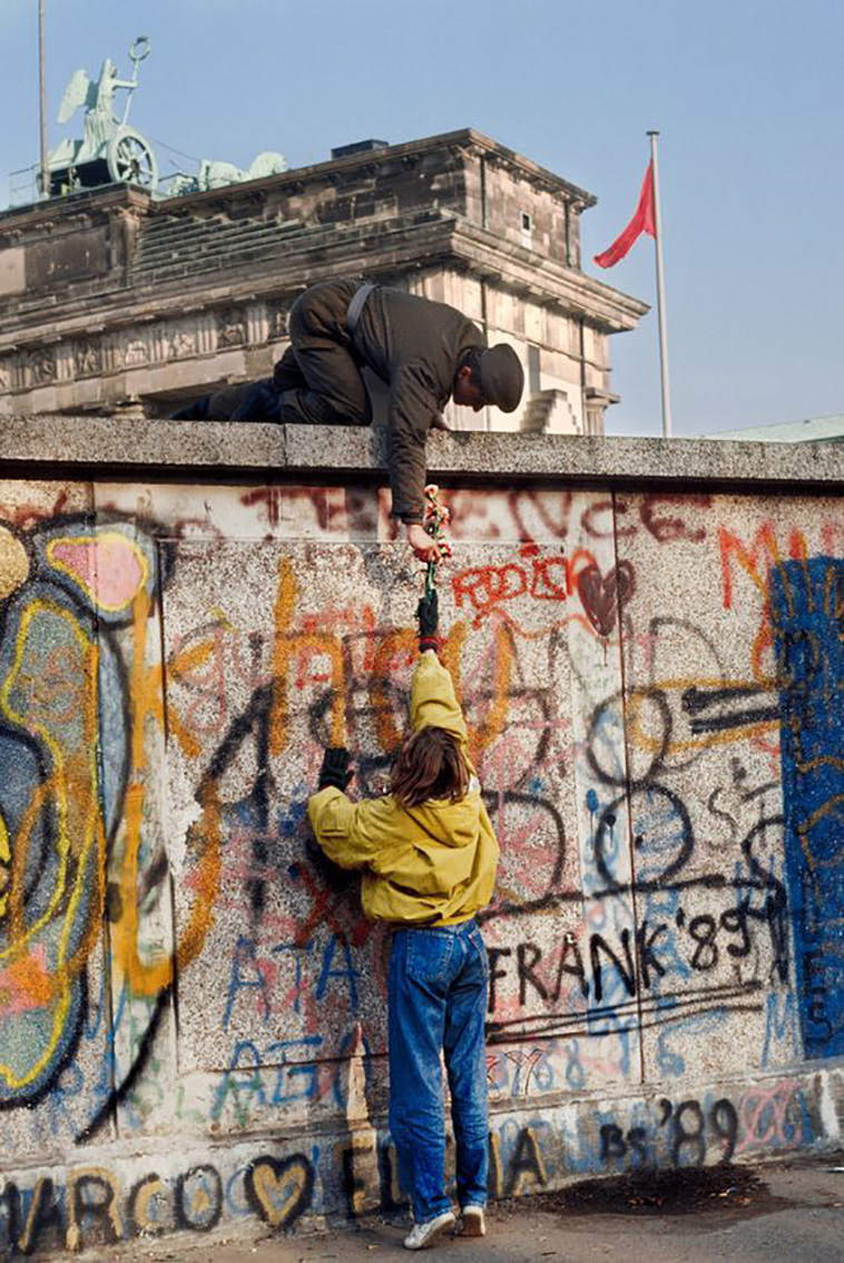 a citizen giving a flower to the soldier on the other side of the Berlin wall